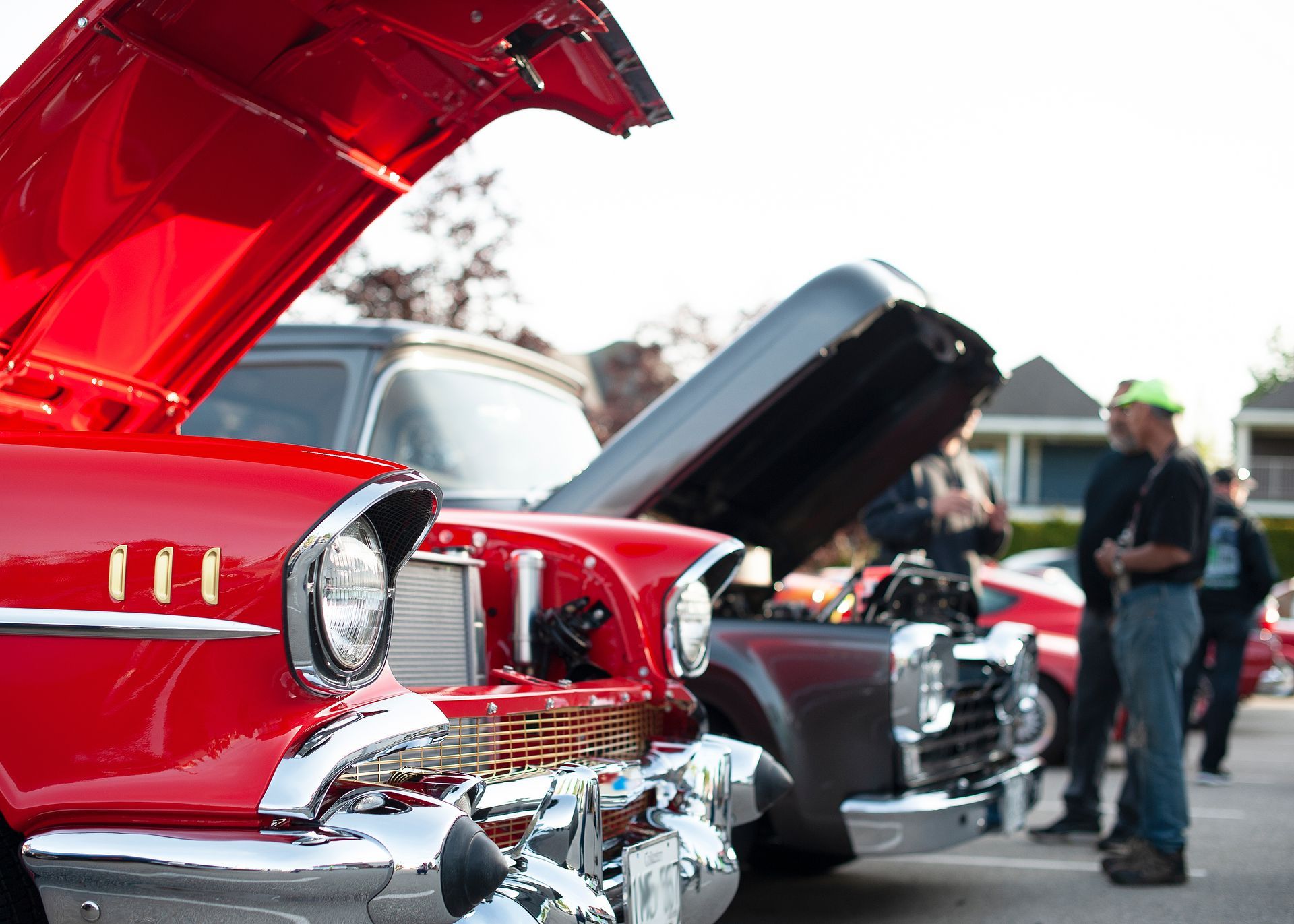 Red and grey classic cars with hoods open at an outdoor car show, people are looking at the engines.