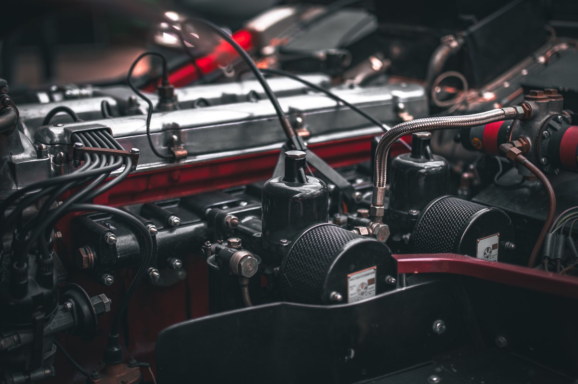 Close-up of a classic car engine with black and silver components, red accents, and visible wiring.