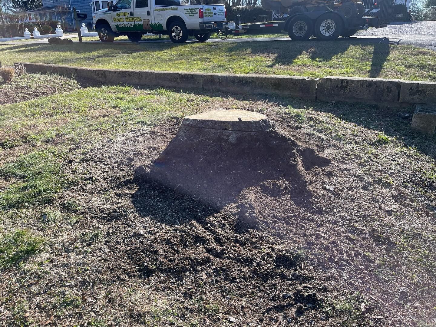 A truck is towing a tree stump in a field.