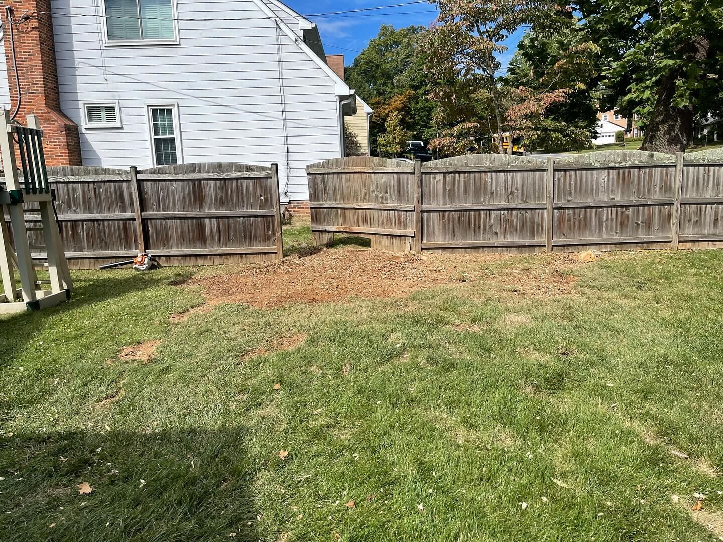 A backyard with a wooden fence and a white house in the background.