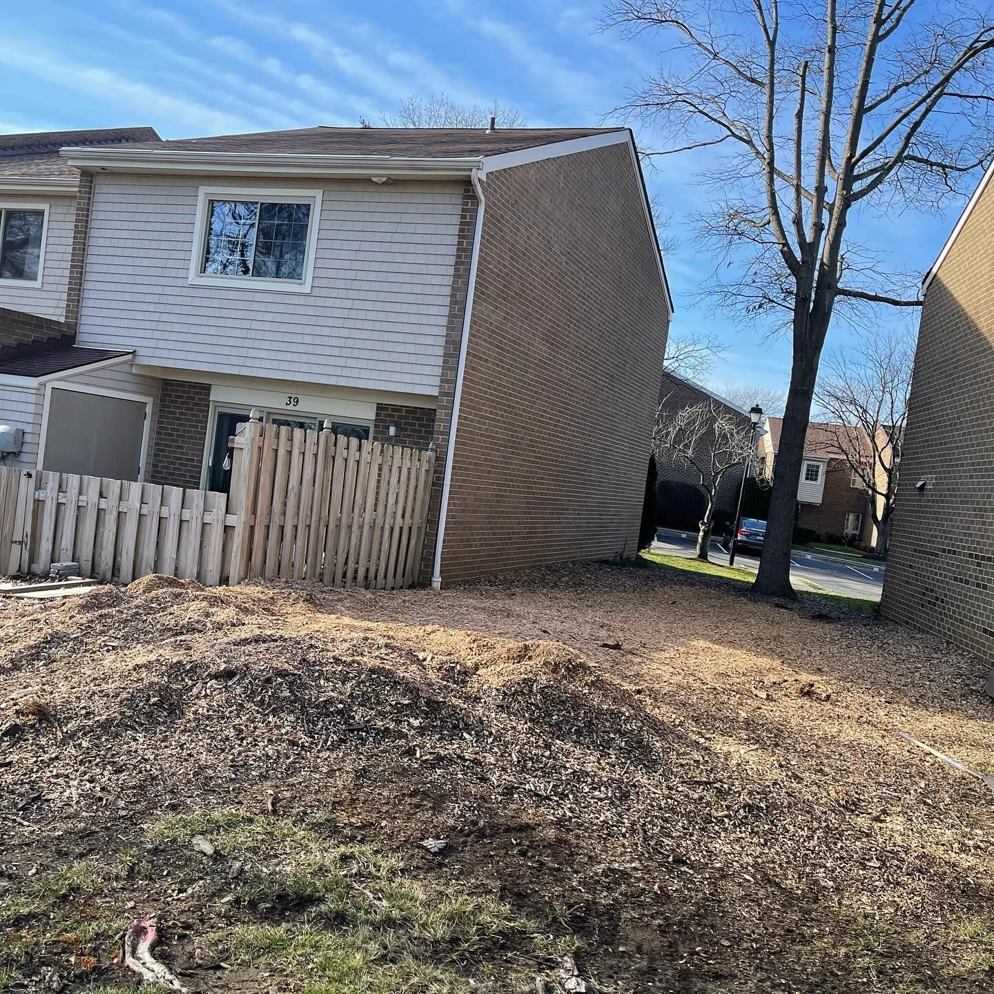 A house with a wooden fence and a tree in front of it.