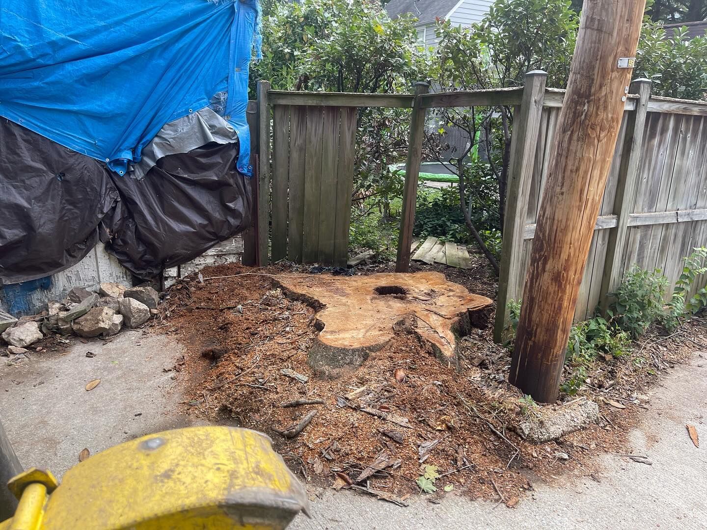 A large tree stump is sitting on the side of the road next to a wooden fence.