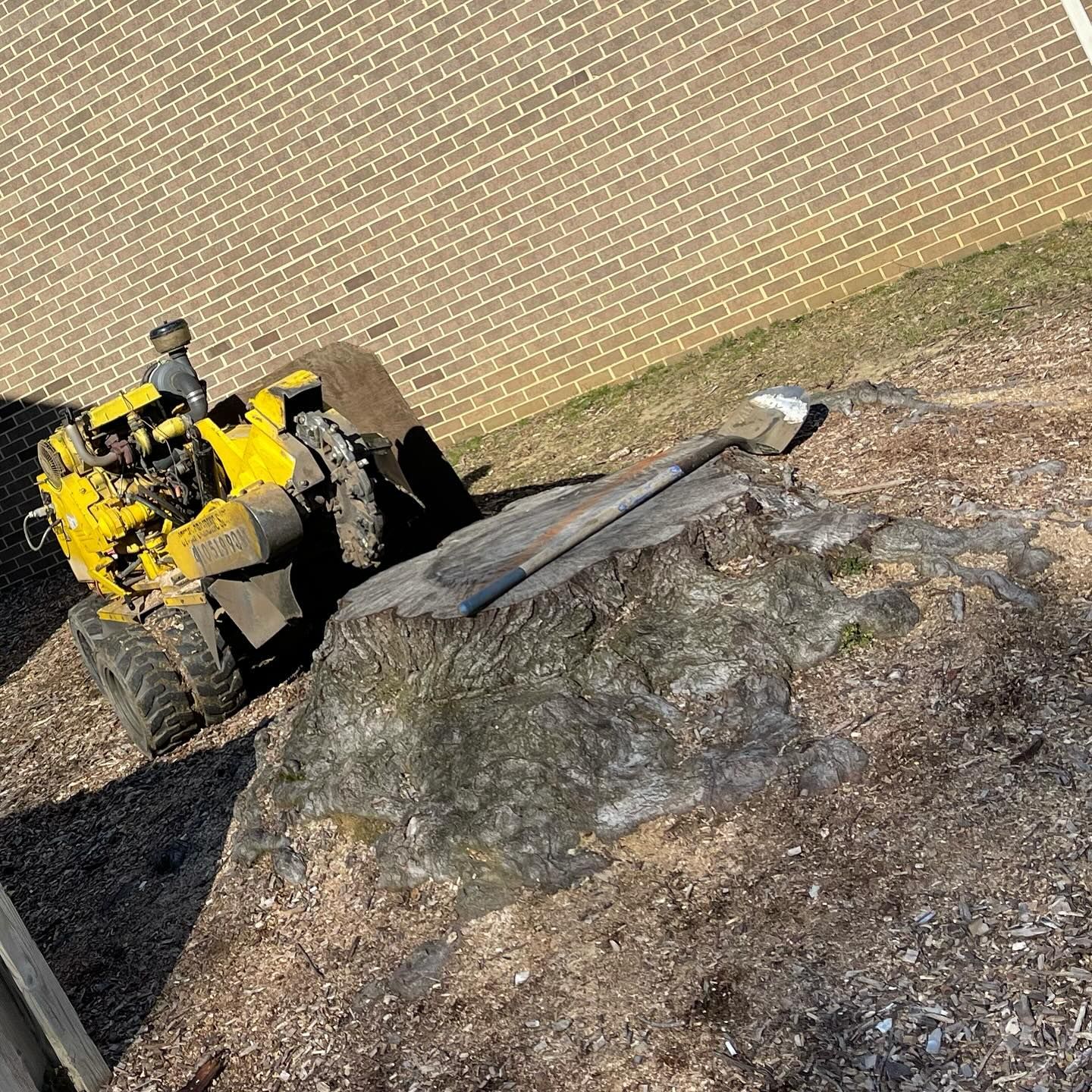 A yellow tractor is sitting on top of a large rock in front of a brick building.