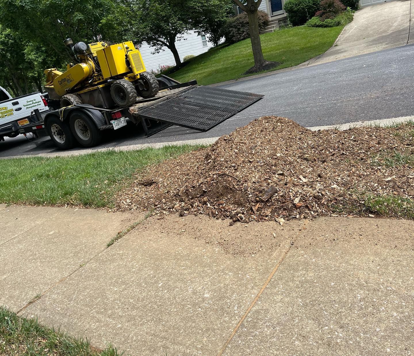 A yellow stump grinder is sitting on top of a trailer.