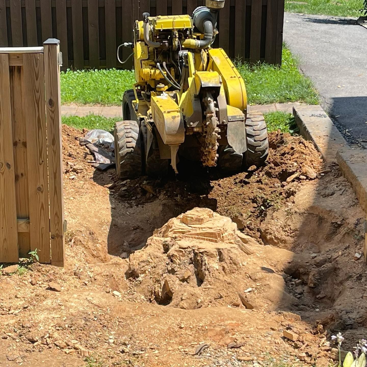 A yellow tractor is digging a hole in the ground next to a wooden fence.