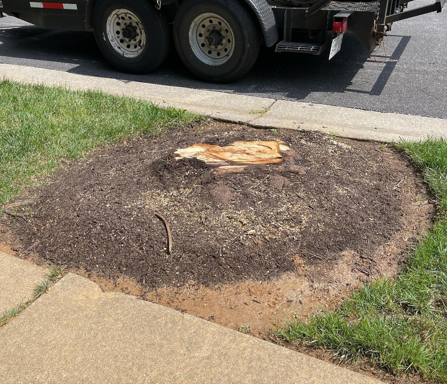 A tree stump is sitting on the sidewalk next to a truck.