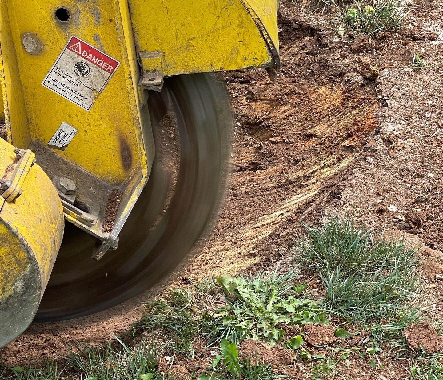 A yellow machine is cutting a tree stump in the dirt.