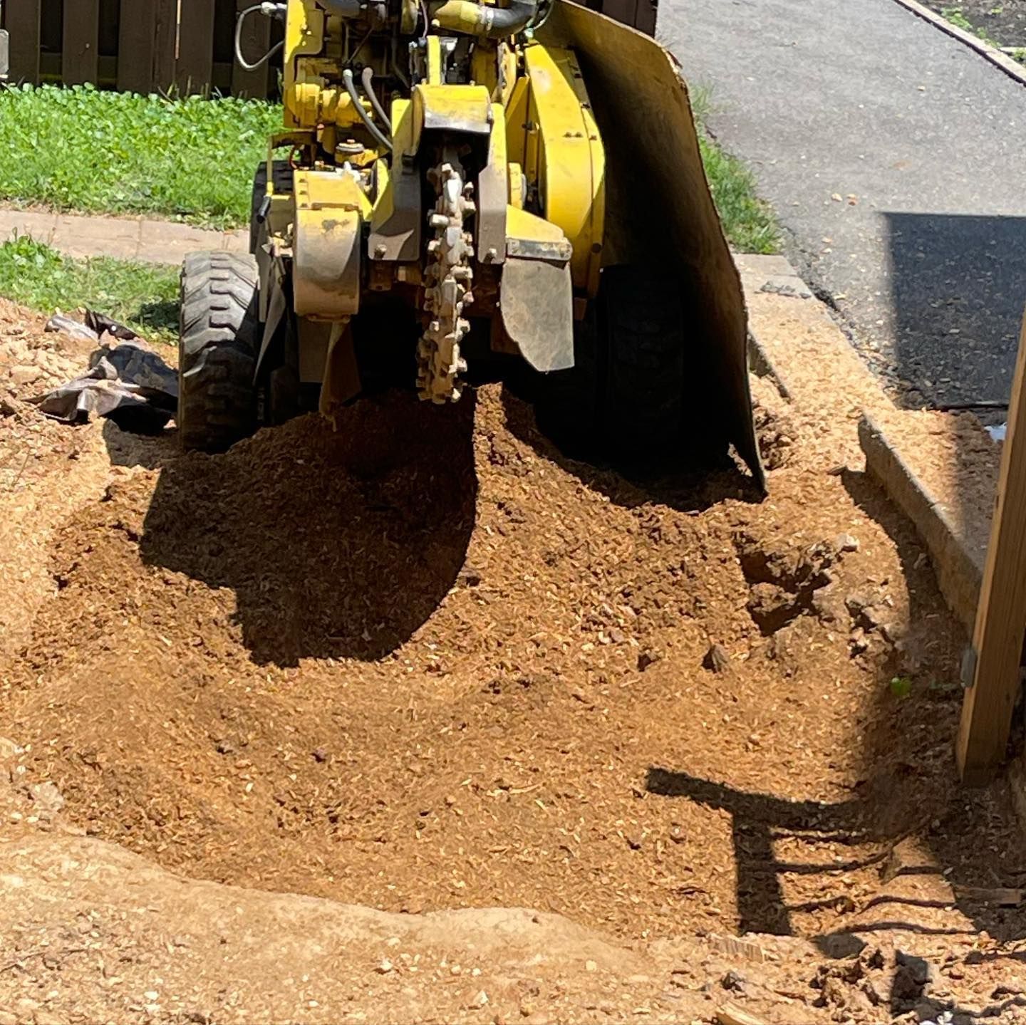 A yellow stump grinder is sitting in a grassy field next to a tree stump.