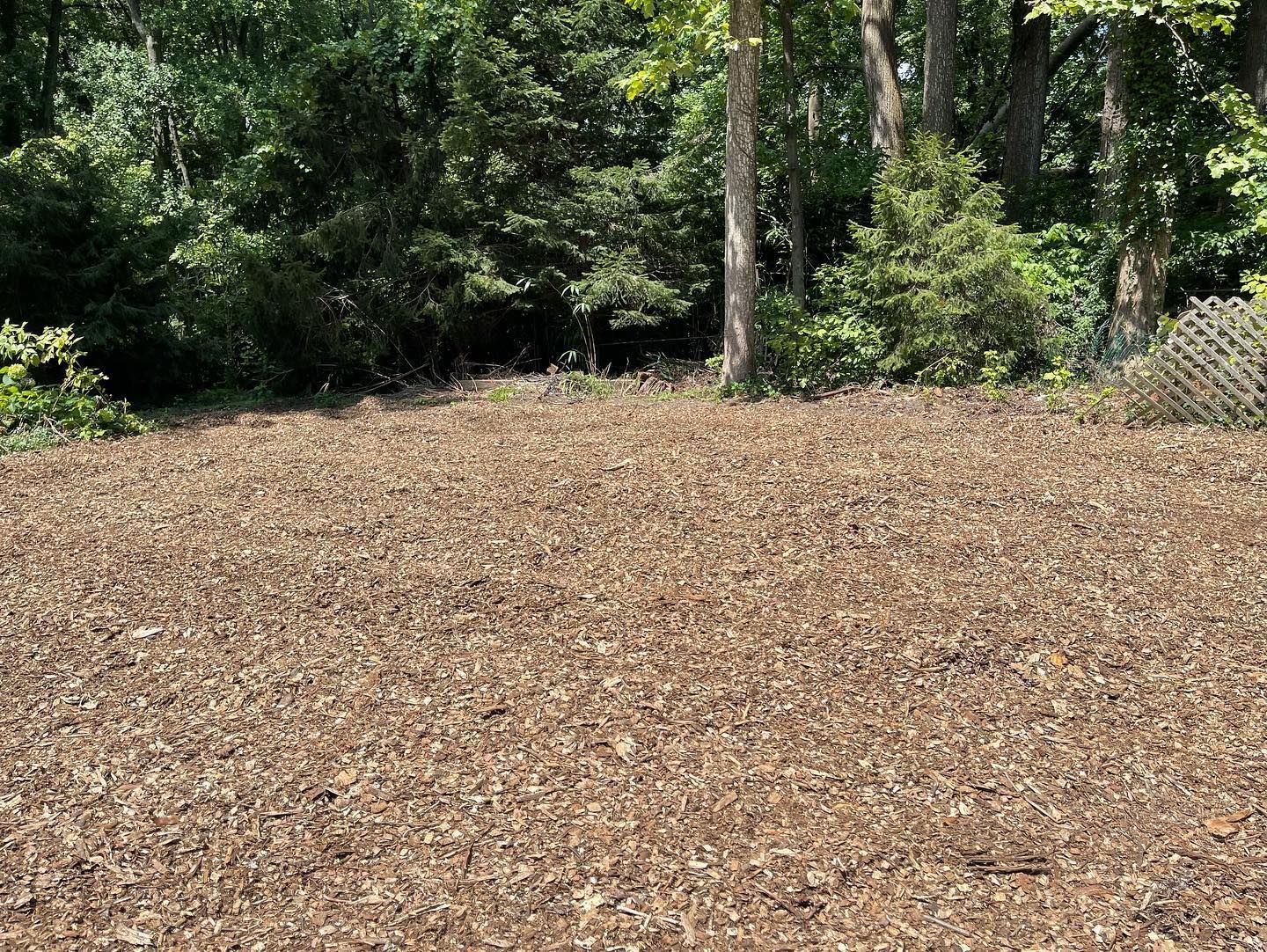 A large pile of brown mulch in a field with trees in the background.