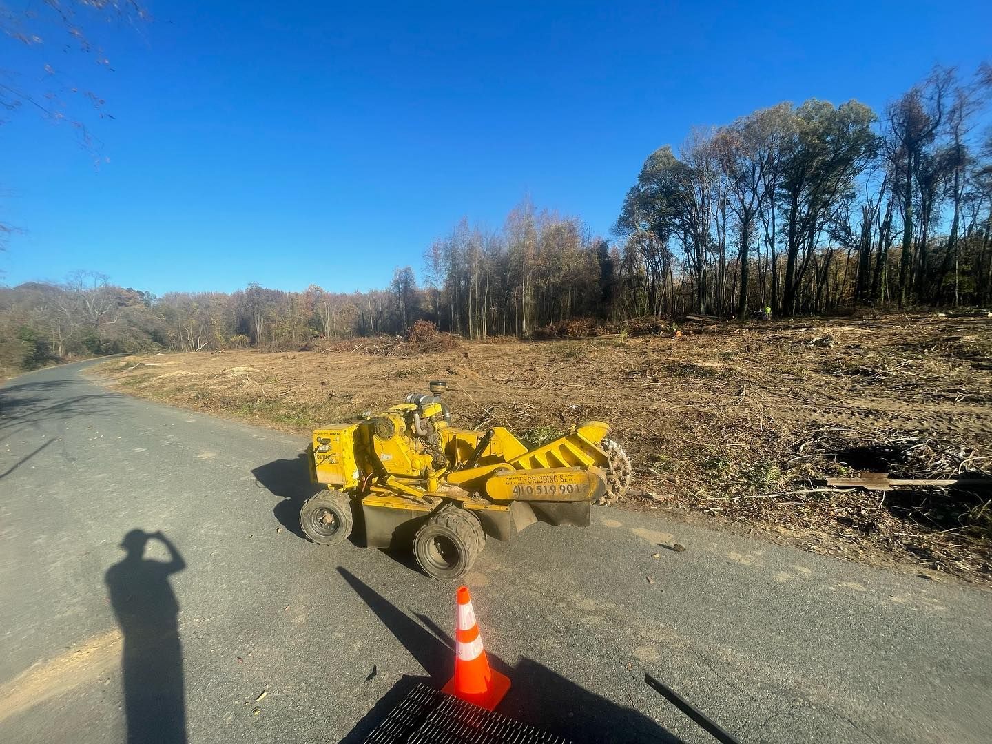 A yellow tractor is sitting on the side of a road next to a traffic cone.