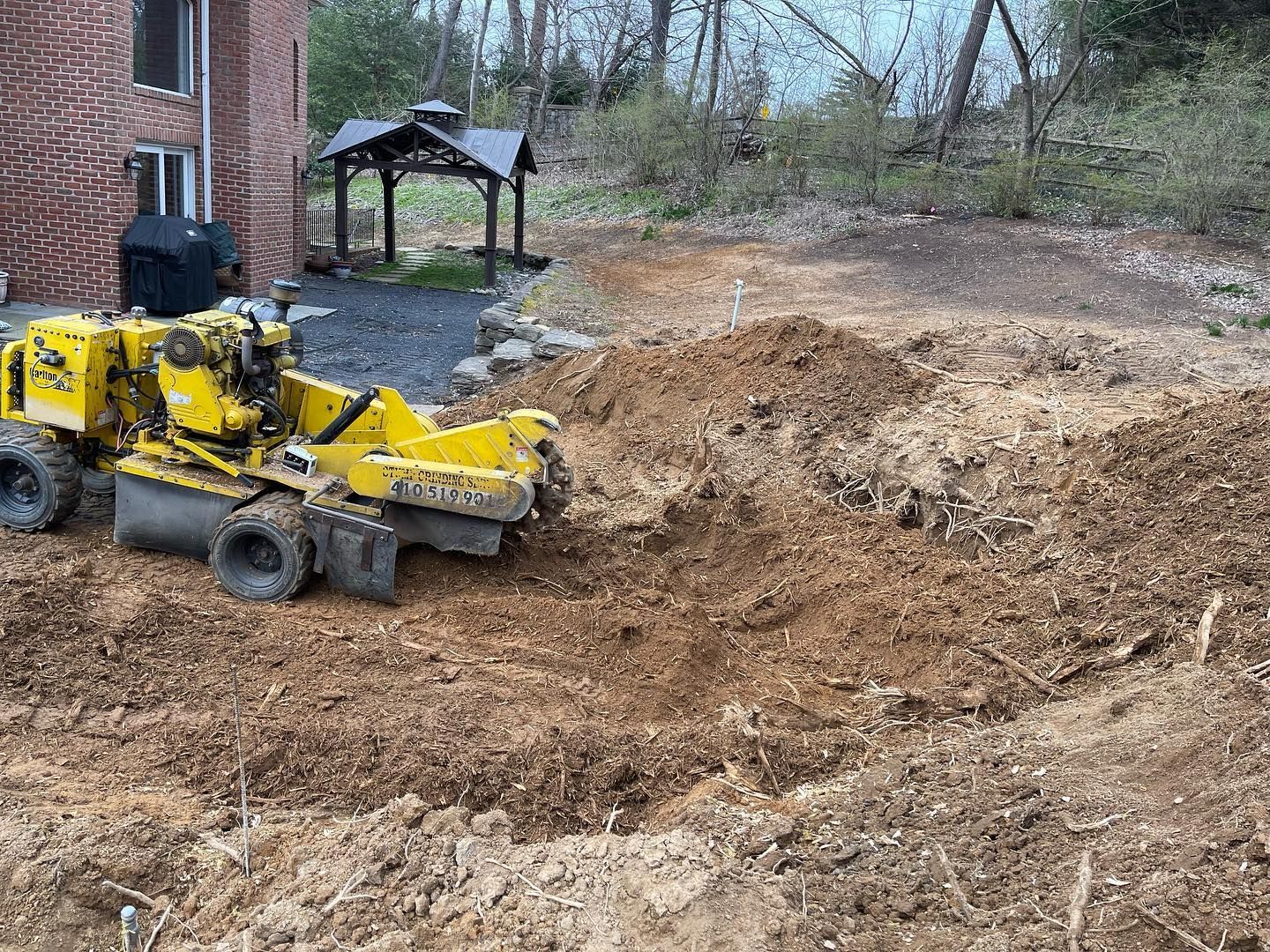 A yellow stump grinder is working on a tree stump in a yard.