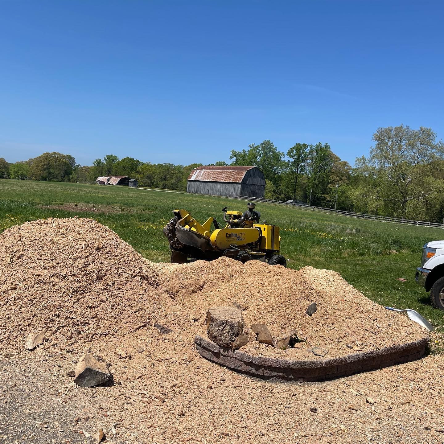 A pile of wood chips next to a stump grinder in a field.