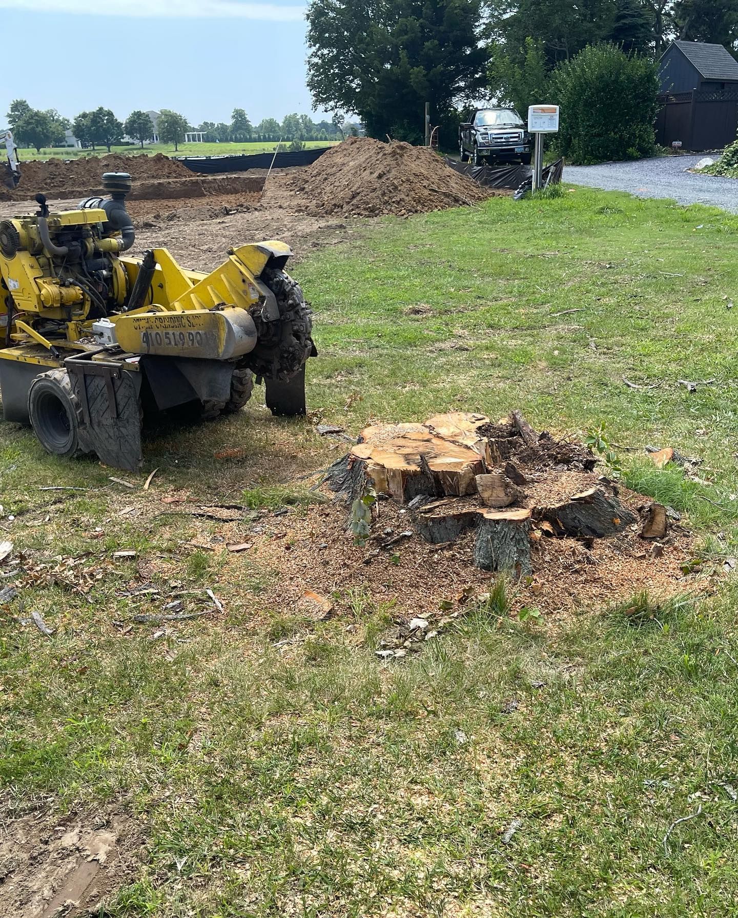 A stump grinder is sitting next to a tree stump in a grassy field.