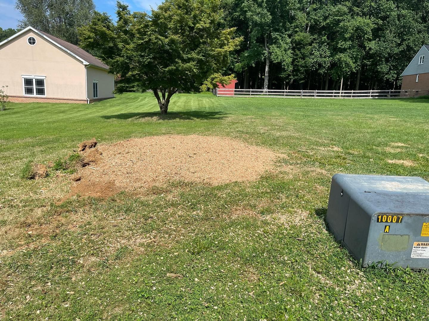A stump in the middle of a lush green field with a house in the background.