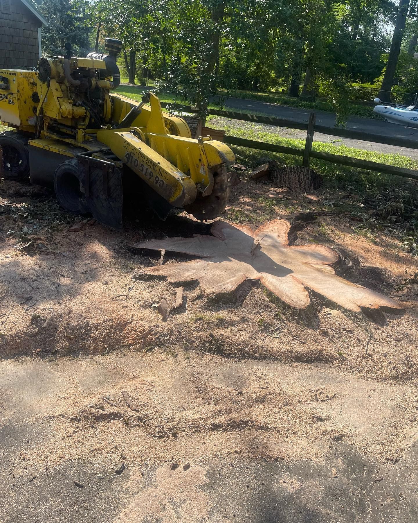 A yellow stump grinder is sitting in the dirt next to a tree stump.
