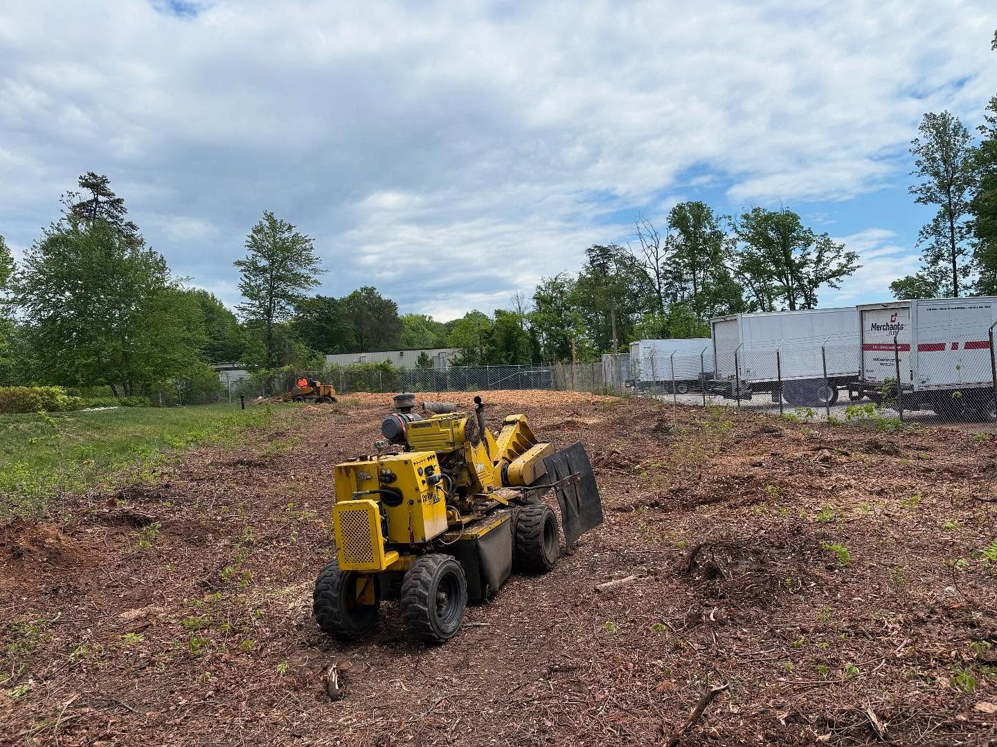 A yellow stump grinder is sitting in the middle of a field.