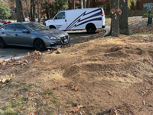 A gray car is parked next to a white van in a dirt lot.