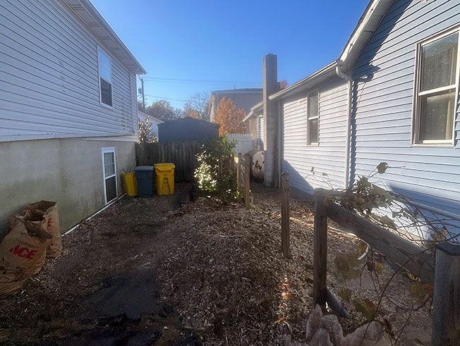 The backyard of a house with a wooden fence and trash cans.