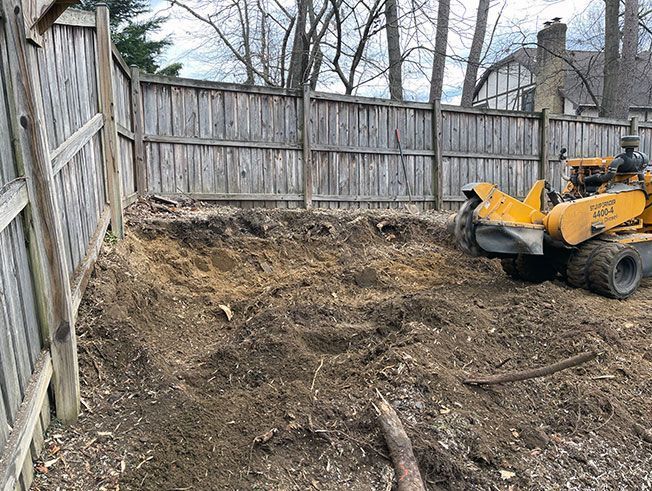 A stump grinder is sitting in a dirt field next to a wooden fence.