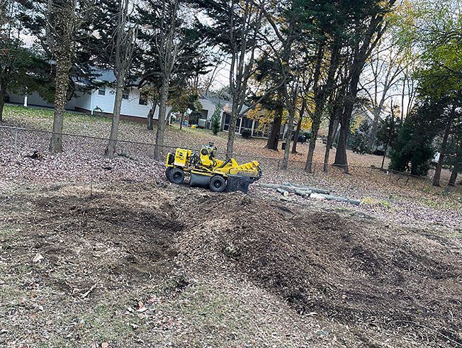 A yellow tractor is driving down a dirt road in a forest.