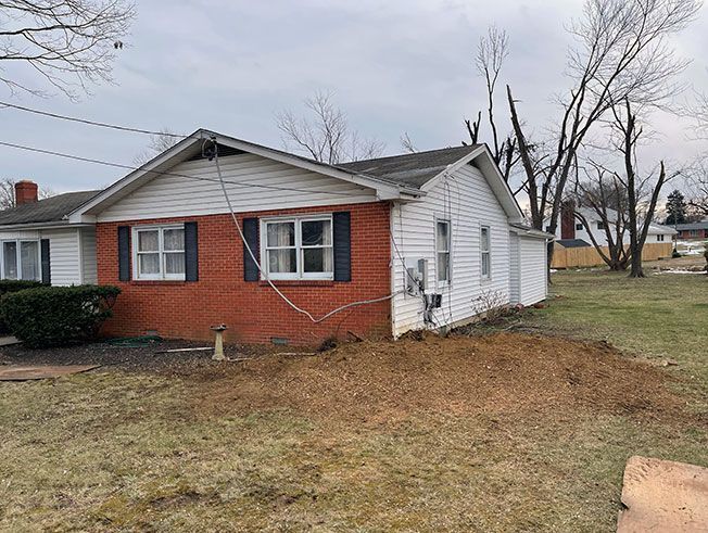 A brick house with a white siding and black shutters is sitting in the middle of a grassy field.