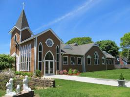 Small brick church with tall white windows, a steeple, and a grassy lawn under a blue sky.