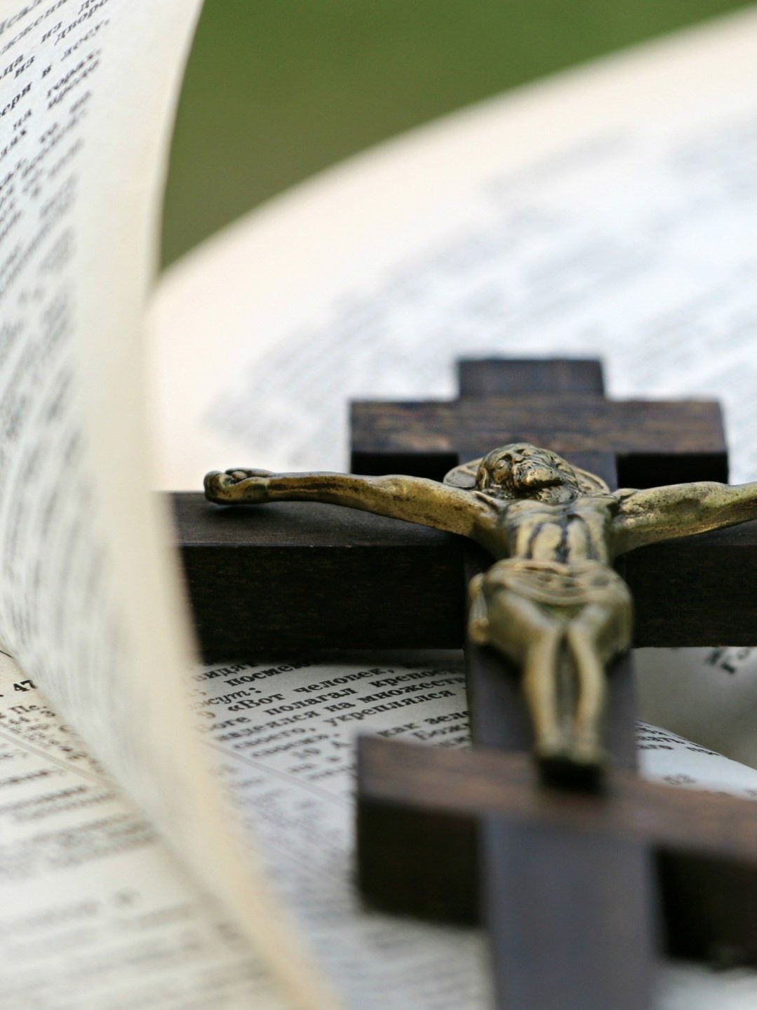 Crucifix resting on an open Bible, framed by a blurred page in the foreground