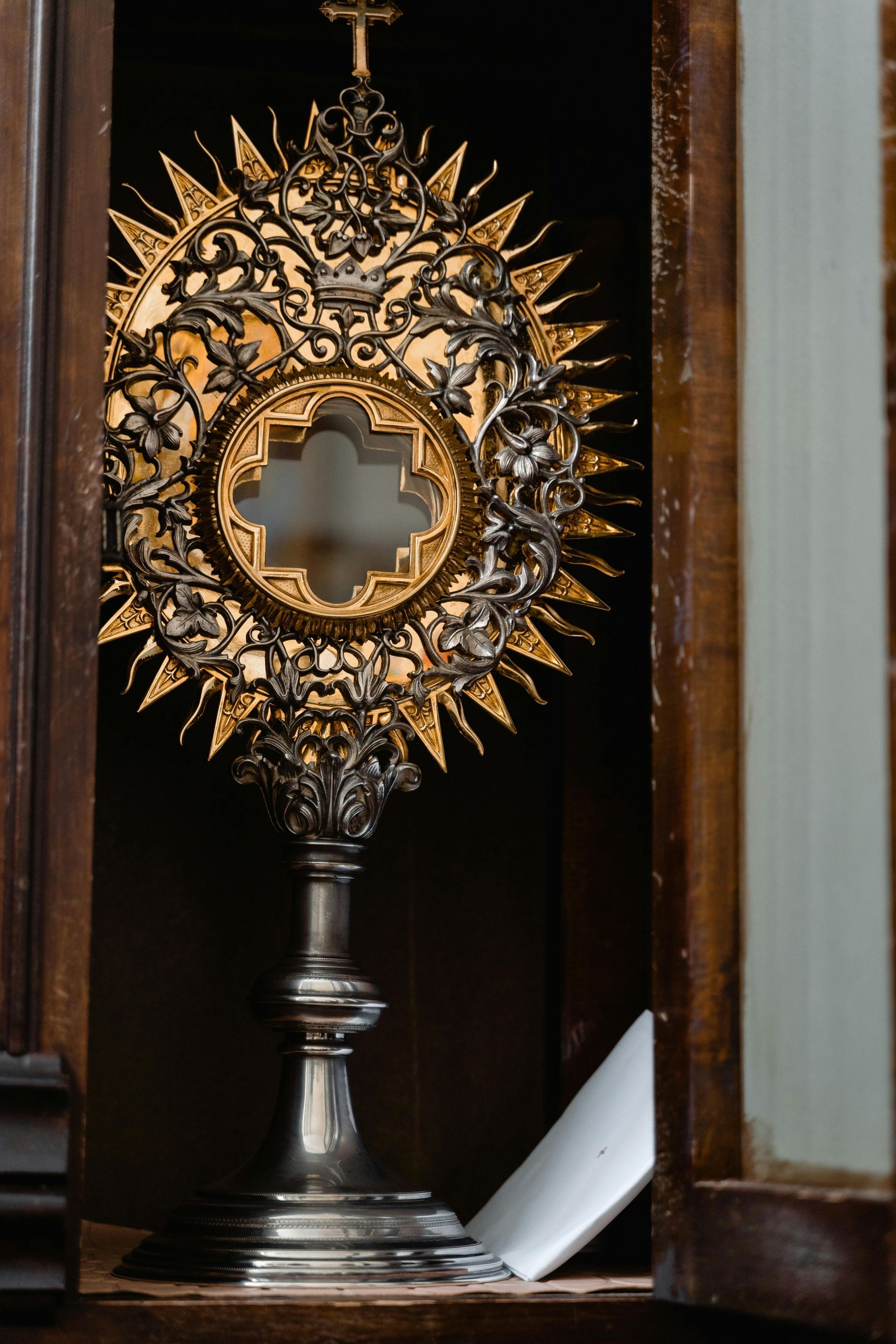 Gold sunburst monstrance with a cross-shaped center on a dark wooden altar
