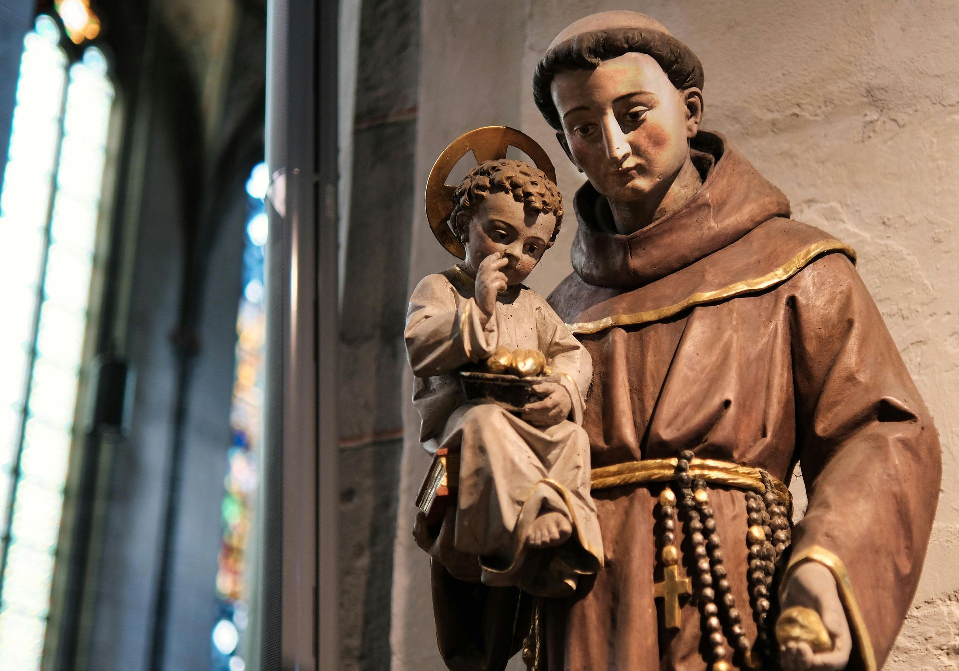 Wooden statue of a saint holding a child beside a stained-glass window