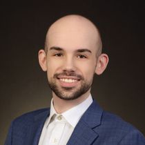 A bald man with a beard wearing a blue suit and white shirt is smiling for the camera.