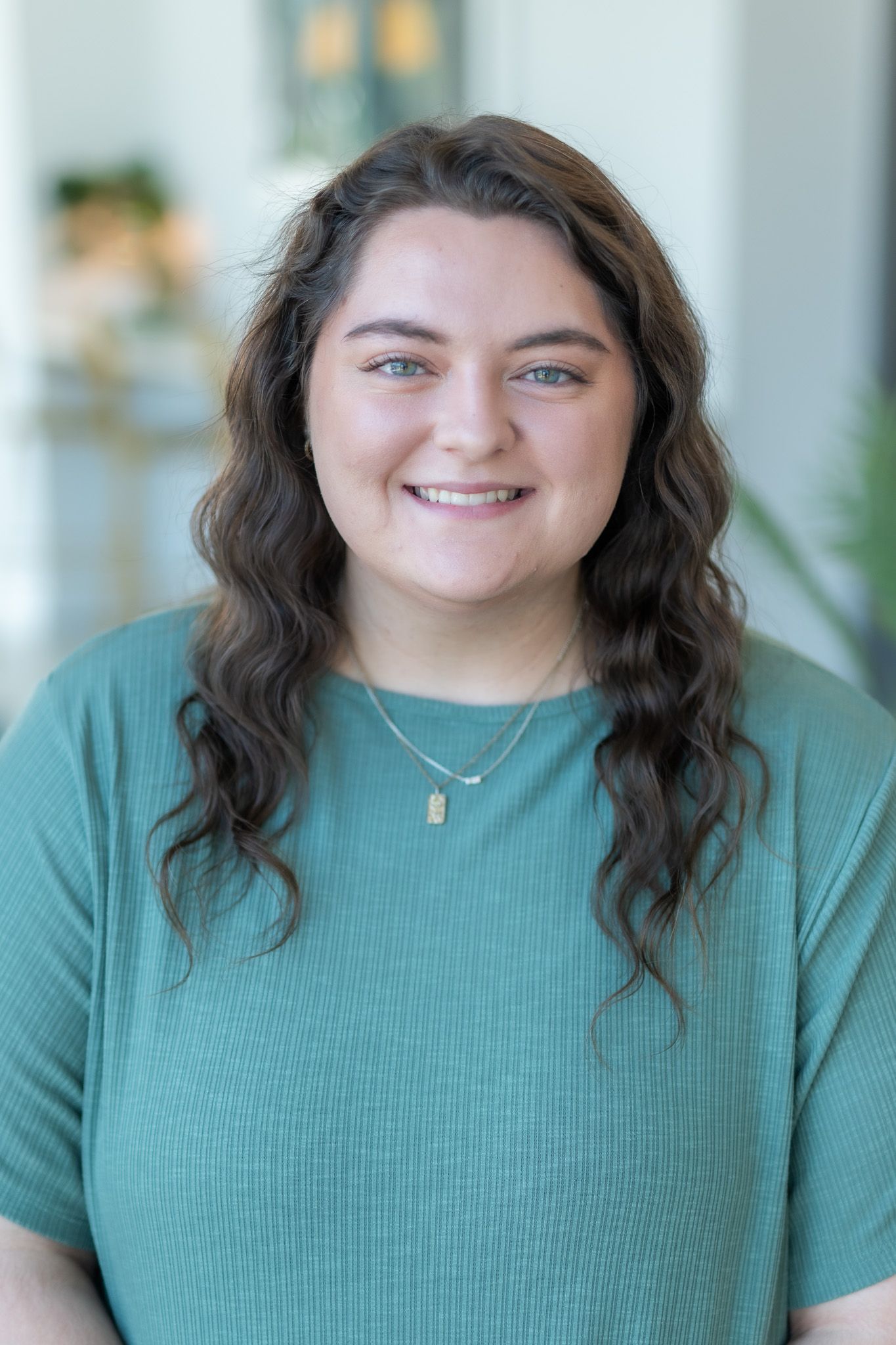 A woman in a green shirt and necklace is smiling for the camera.