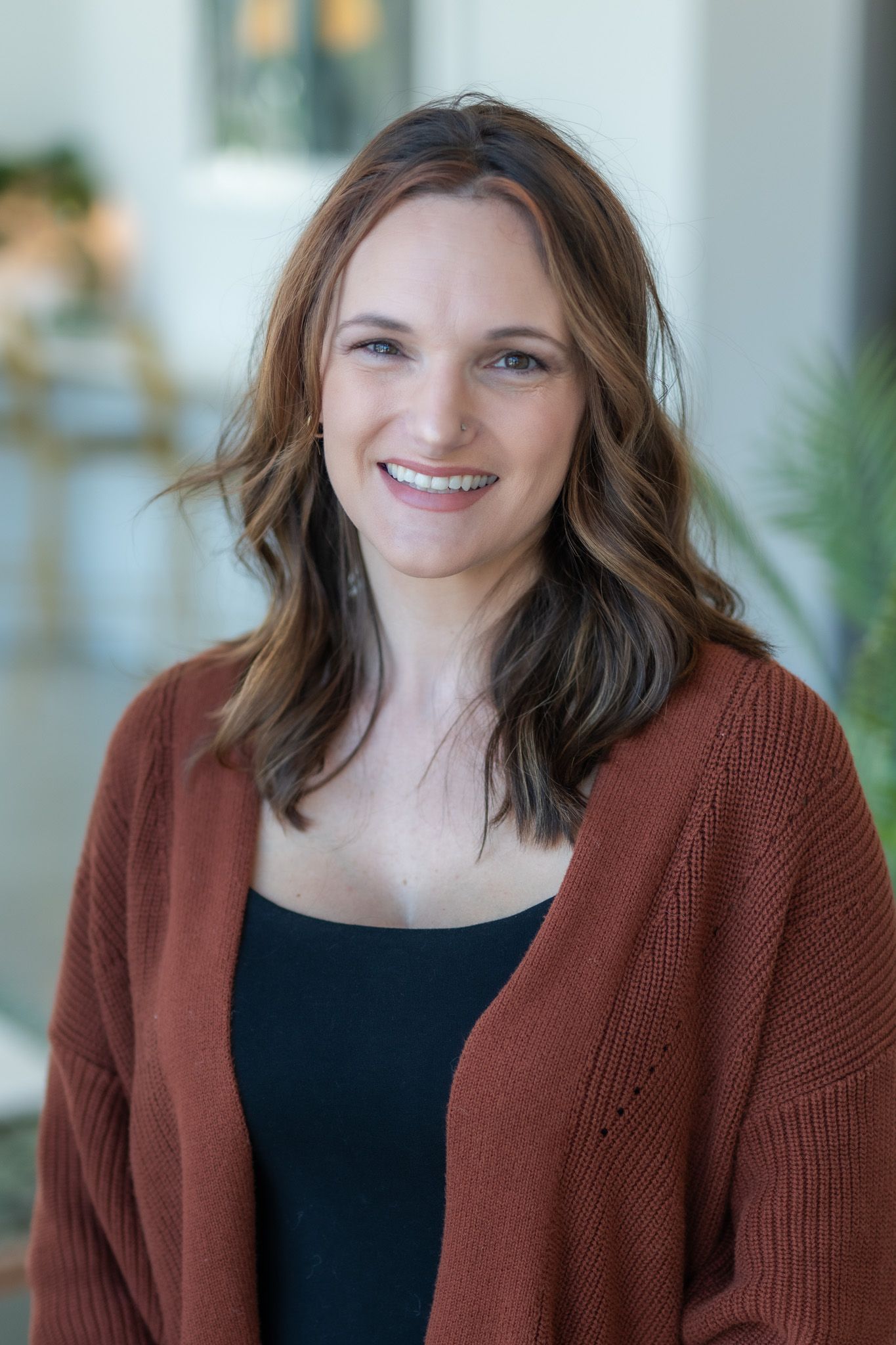 A woman wearing a brown cardigan and a black tank top is smiling for the camera.