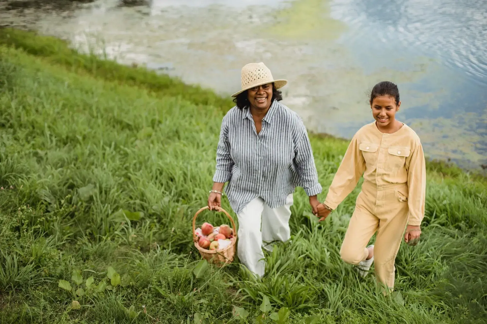 An elderly woman and a young girl are walking in a field holding hands.