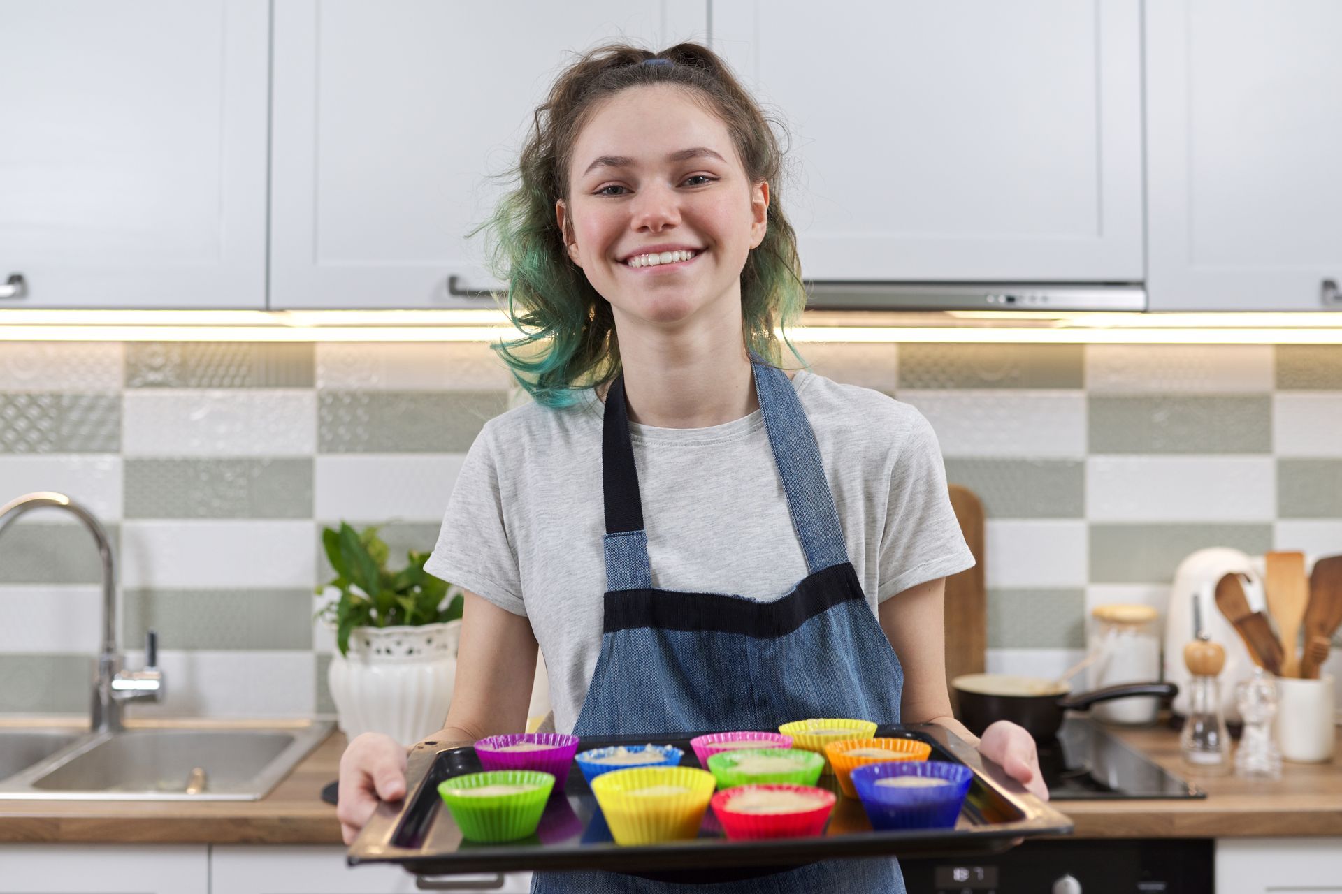 A woman is holding a tray of cupcakes in a kitchen.