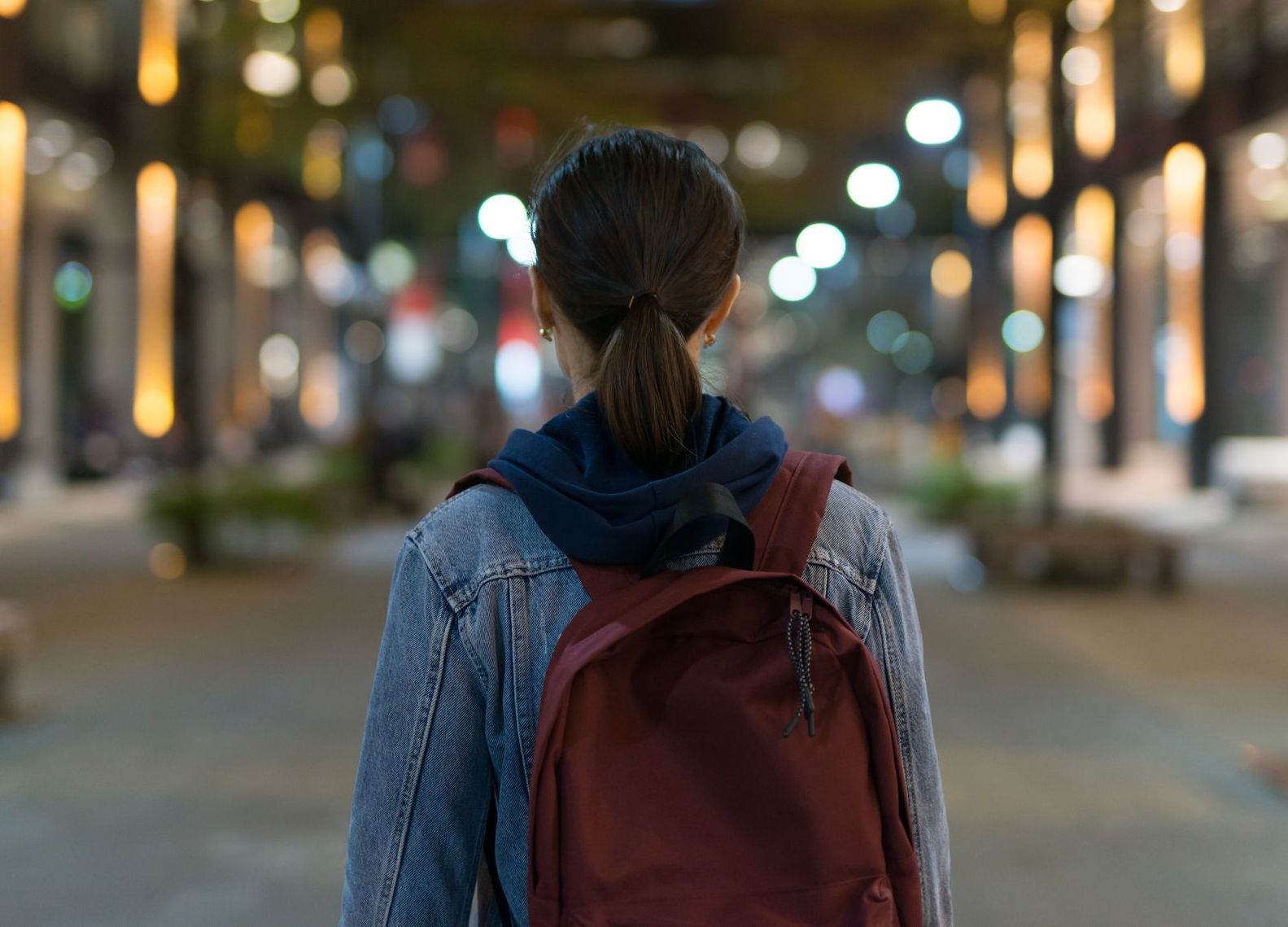 A woman with a backpack is walking down a city street at night.