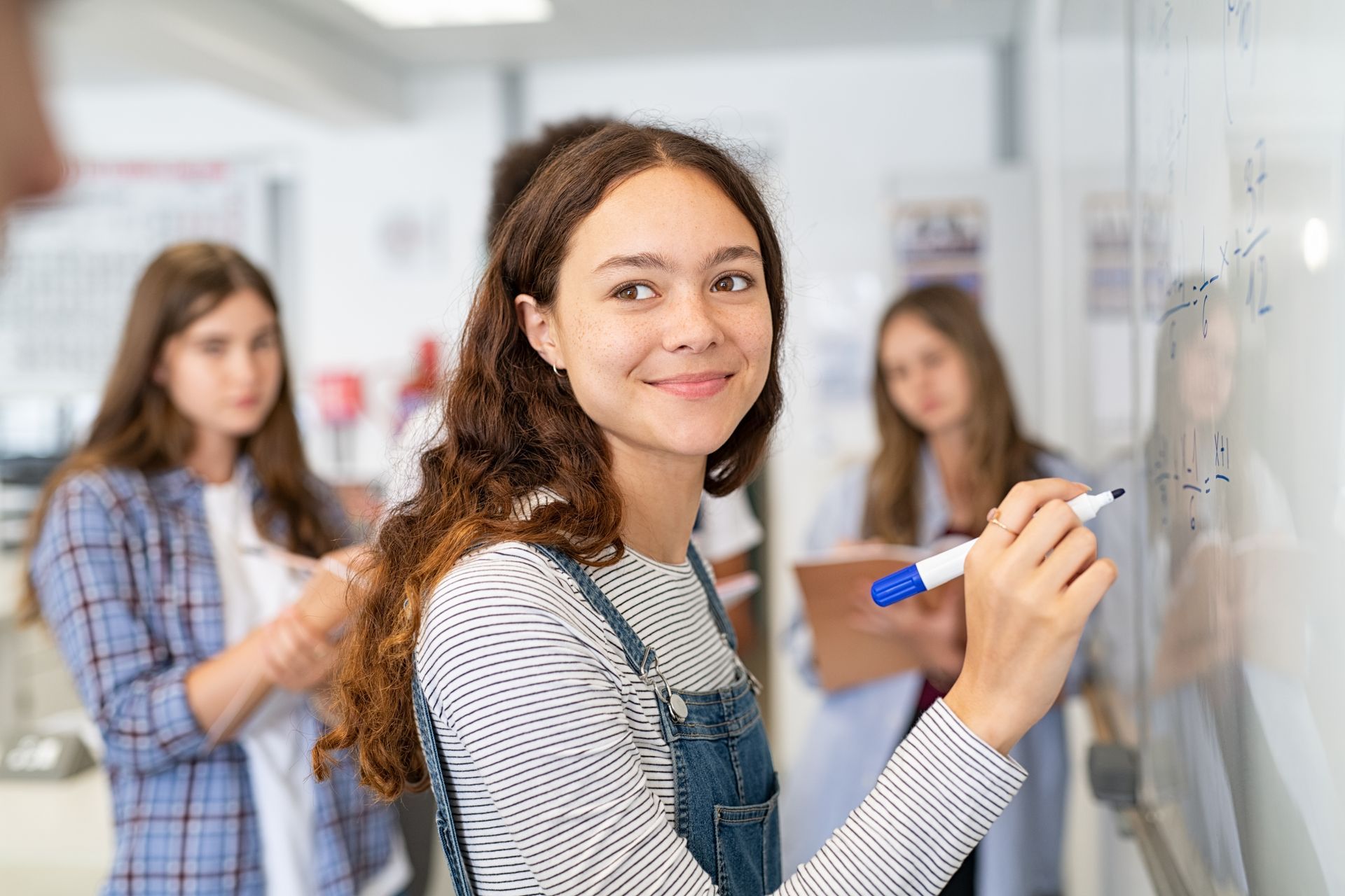 A young girl is writing on a whiteboard in a classroom.