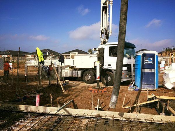 Concrete truck pumping concrete into a foundation form on a construction site with a portable toilet
