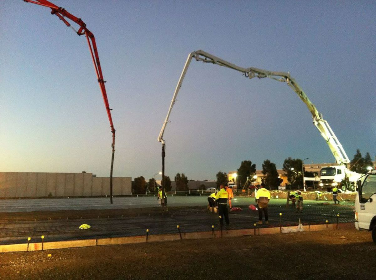 Construction workers pour concrete with boom pumps at dusk.