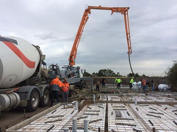 Construction site with concrete being poured from a truck-mounted boom into a foundation. Workers in
