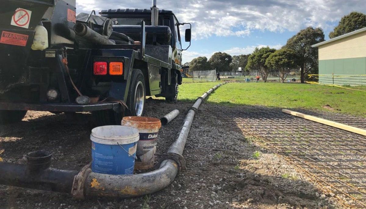 Concrete truck with a hose delivering concrete to a construction site on a grassy field.