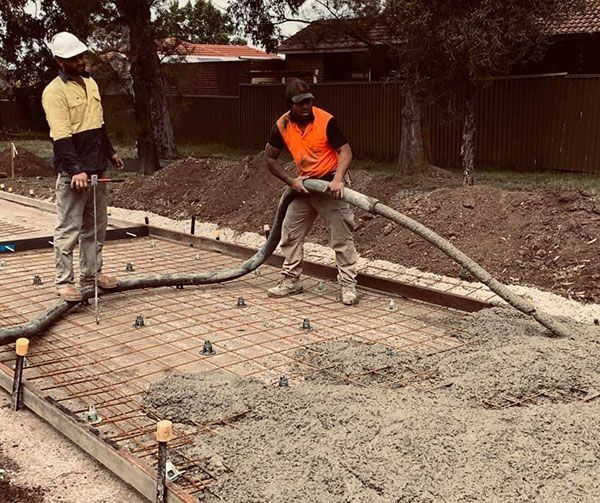 Two construction workers pouring concrete onto rebar framework outdoors.