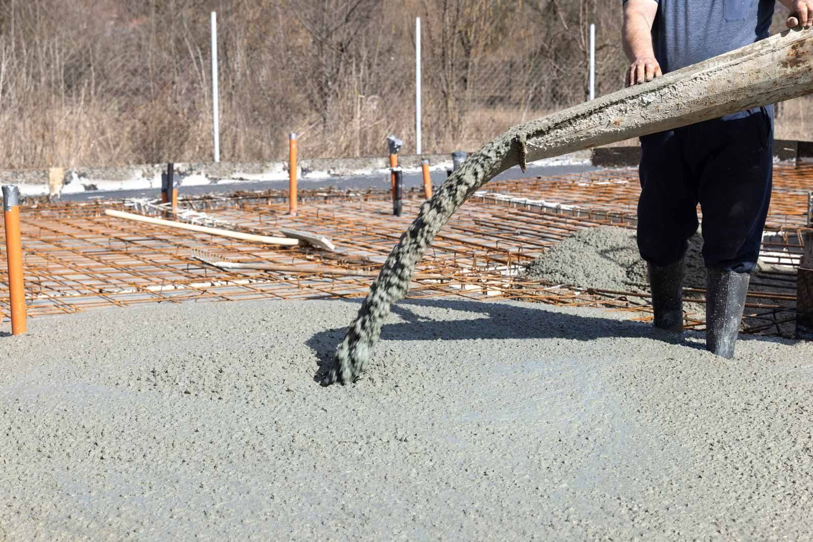 Person pouring wet concrete from a chute onto a rebar-reinforced surface outdoors.
