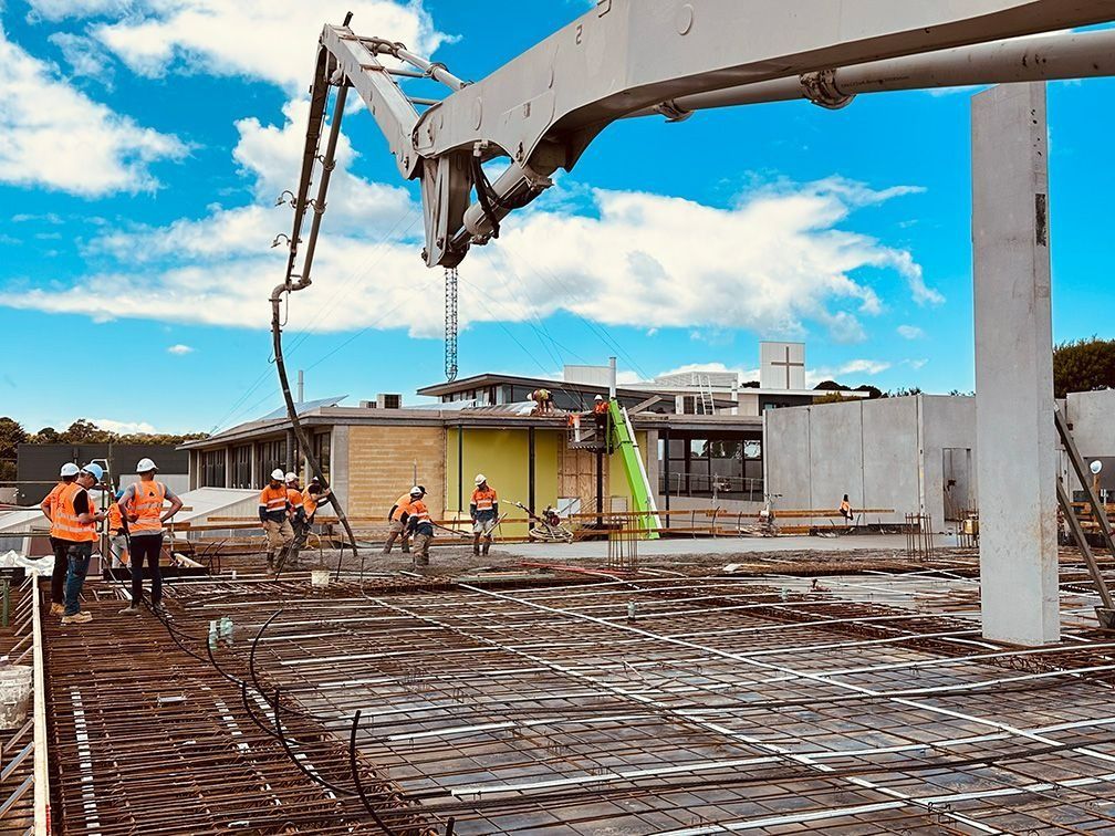 Construction site with workers pouring concrete for a building foundation under a blue sky.