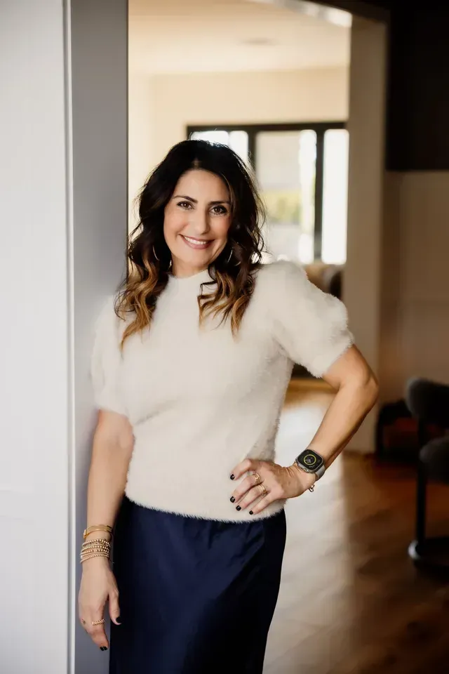 Mania Persekian, REALTOR, top real estate agent in Orange County, posing in a white top in a doorway.