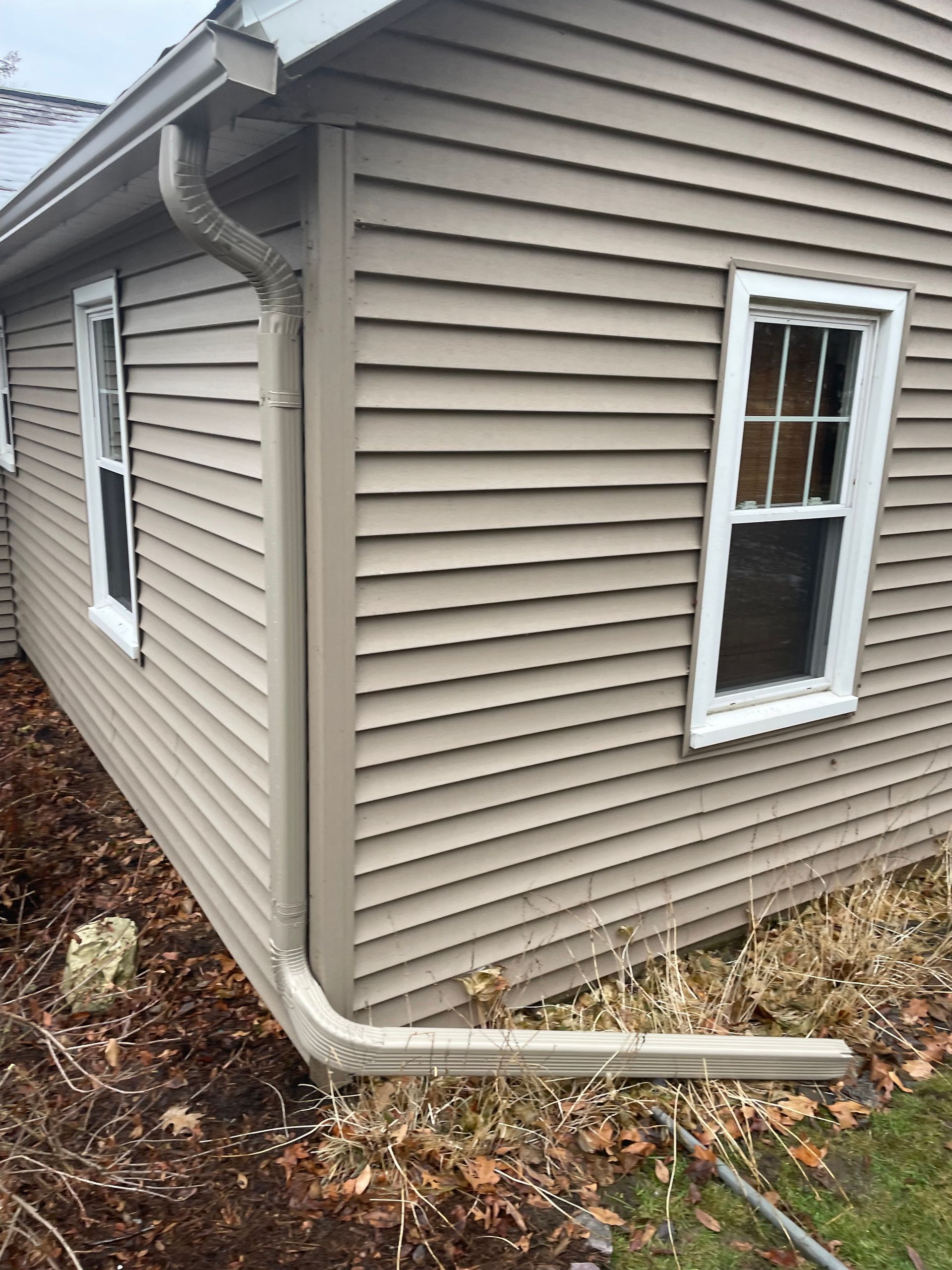 A house with a gutter on the side of it and two windows.