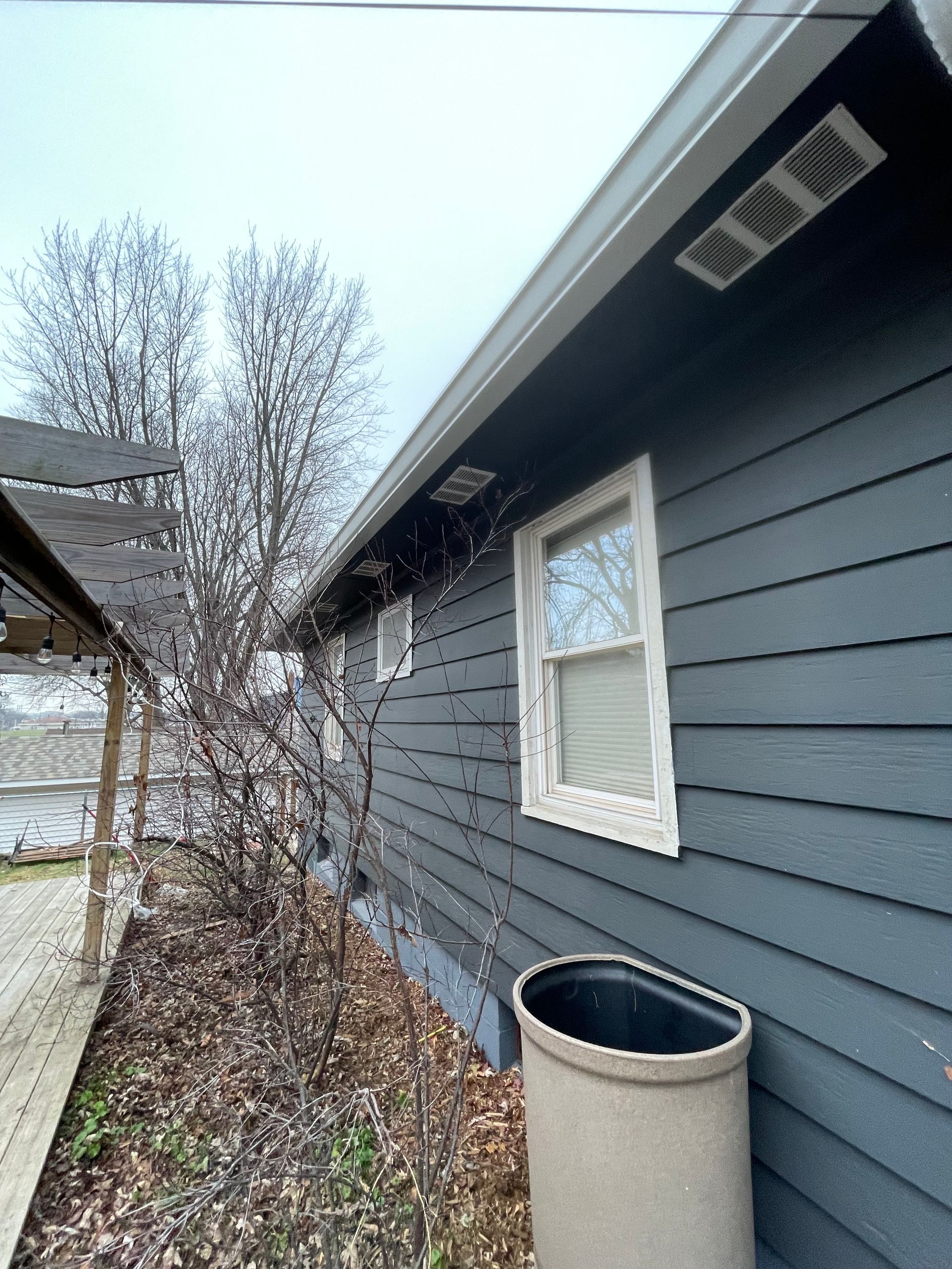 A house with a gray siding and white windows has a concrete planter in front of it.
