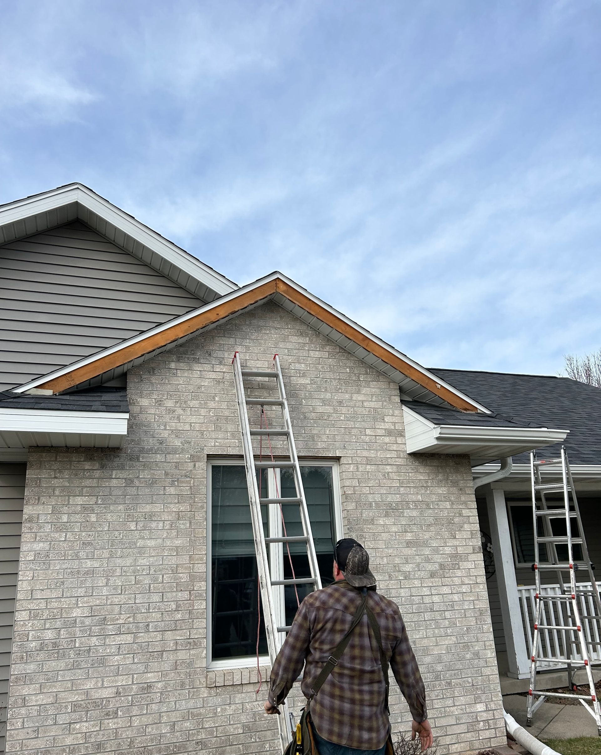 A man is standing in front of a brick house with a ladder.