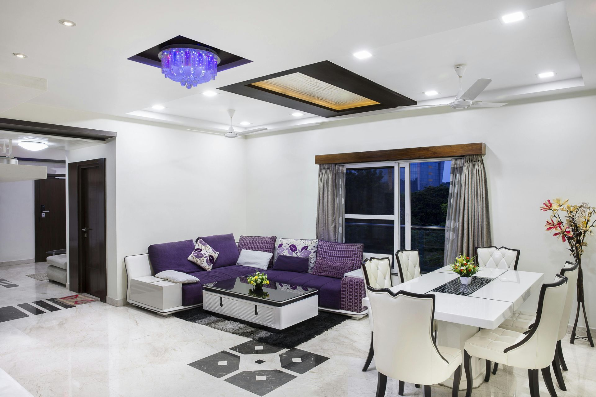 Living room with purple sectional, white dining table, and ornate ceiling lights.