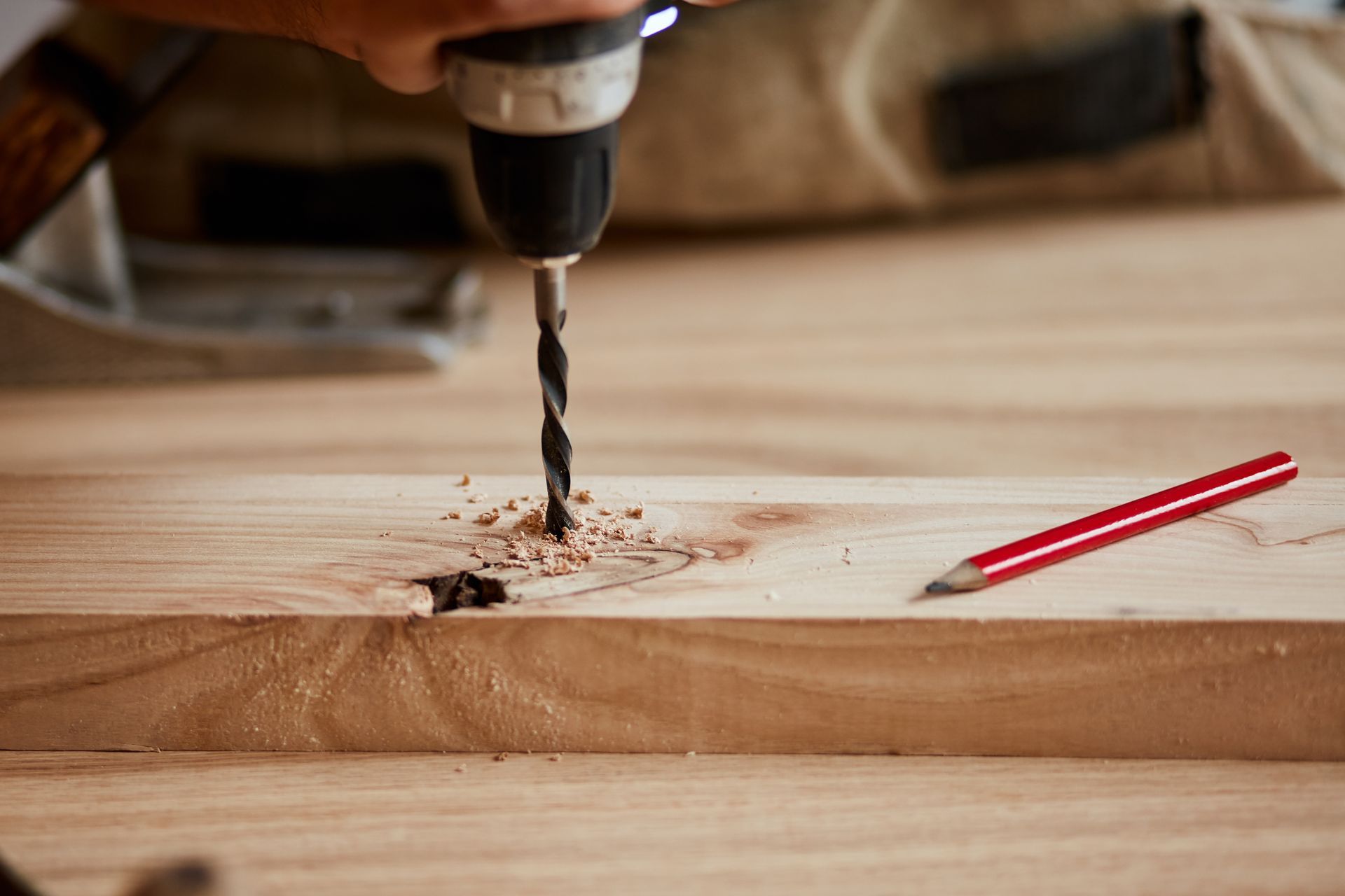 Drill boring into wood, sawdust flying. Pencil rests nearby.