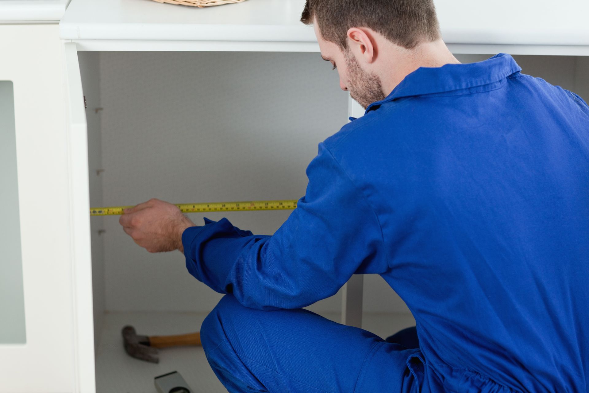 Person measuring cabinet interior with tape measure during home renovation and kitchen remodel work.